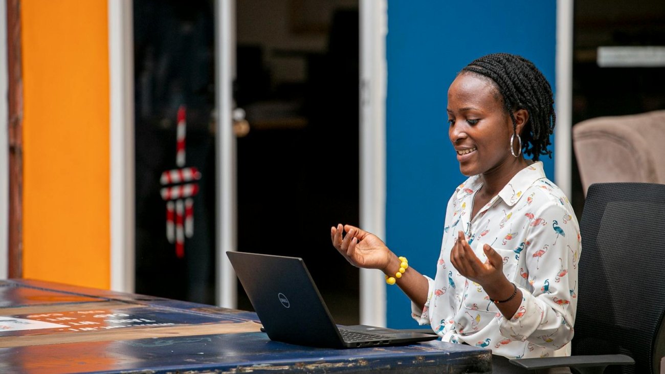 Smiling African woman with dreadlocks having an online video call in a colorful office.