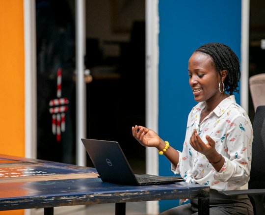 Smiling African woman with dreadlocks having an online video call in a colorful office.
